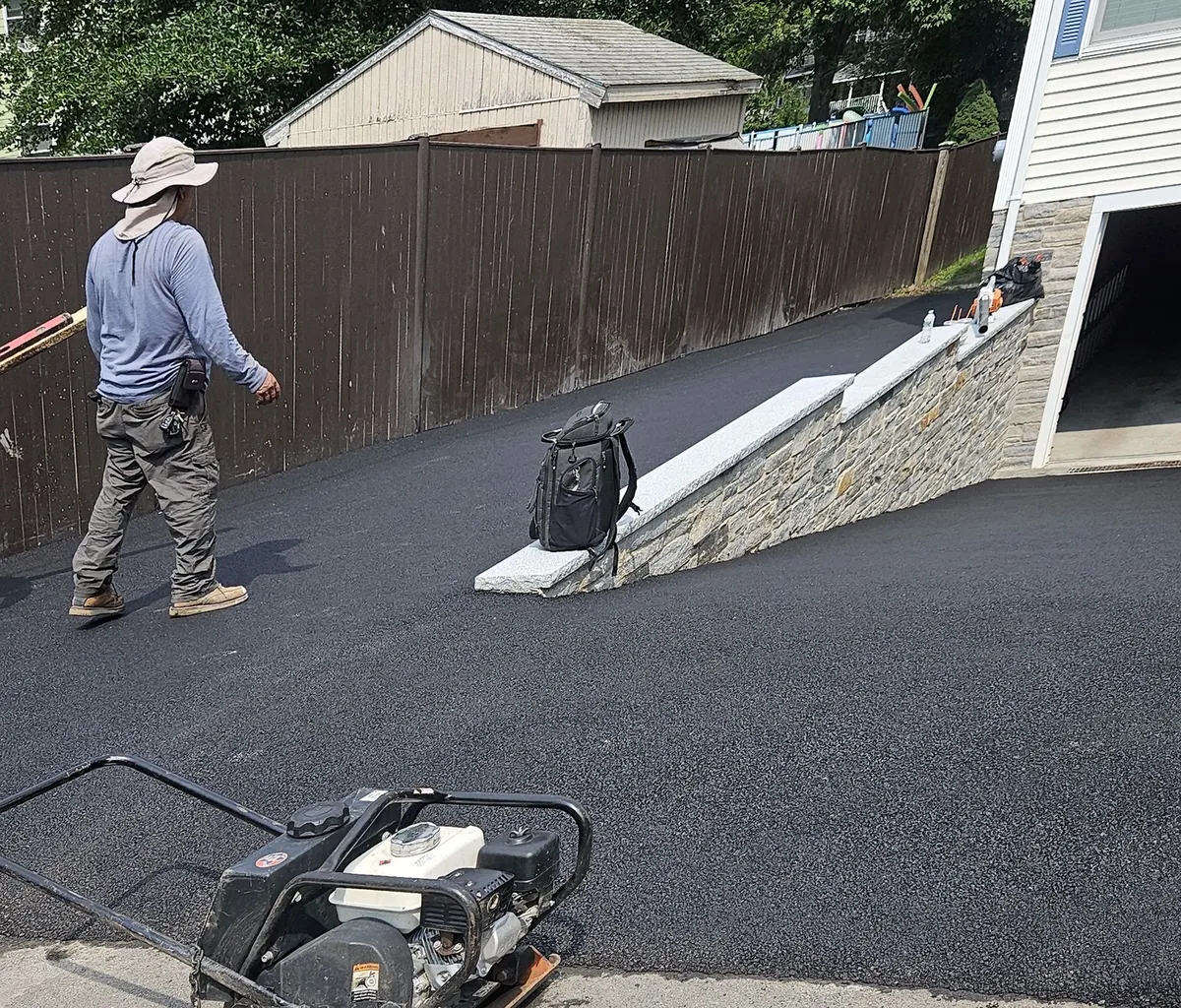 Crew finishing a new asphalt driveway beside a stone retaining wall